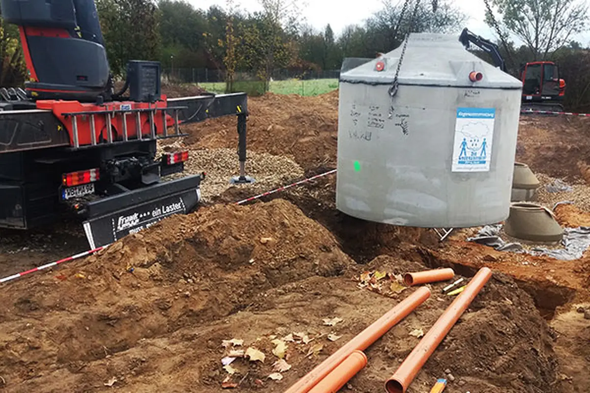 Betonzisterne wird per Kran in die ausgehobene Baugrube gesetz