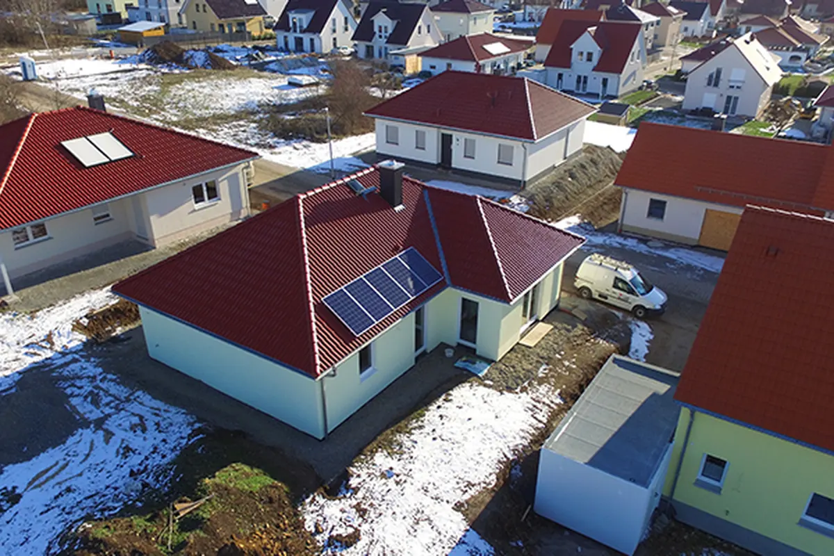 Fertiggestellter Bungalow mit dunkelrotem Walmdach und Photovoltaikanlage nach dem Außenputz – Luftaufnahme im Winter