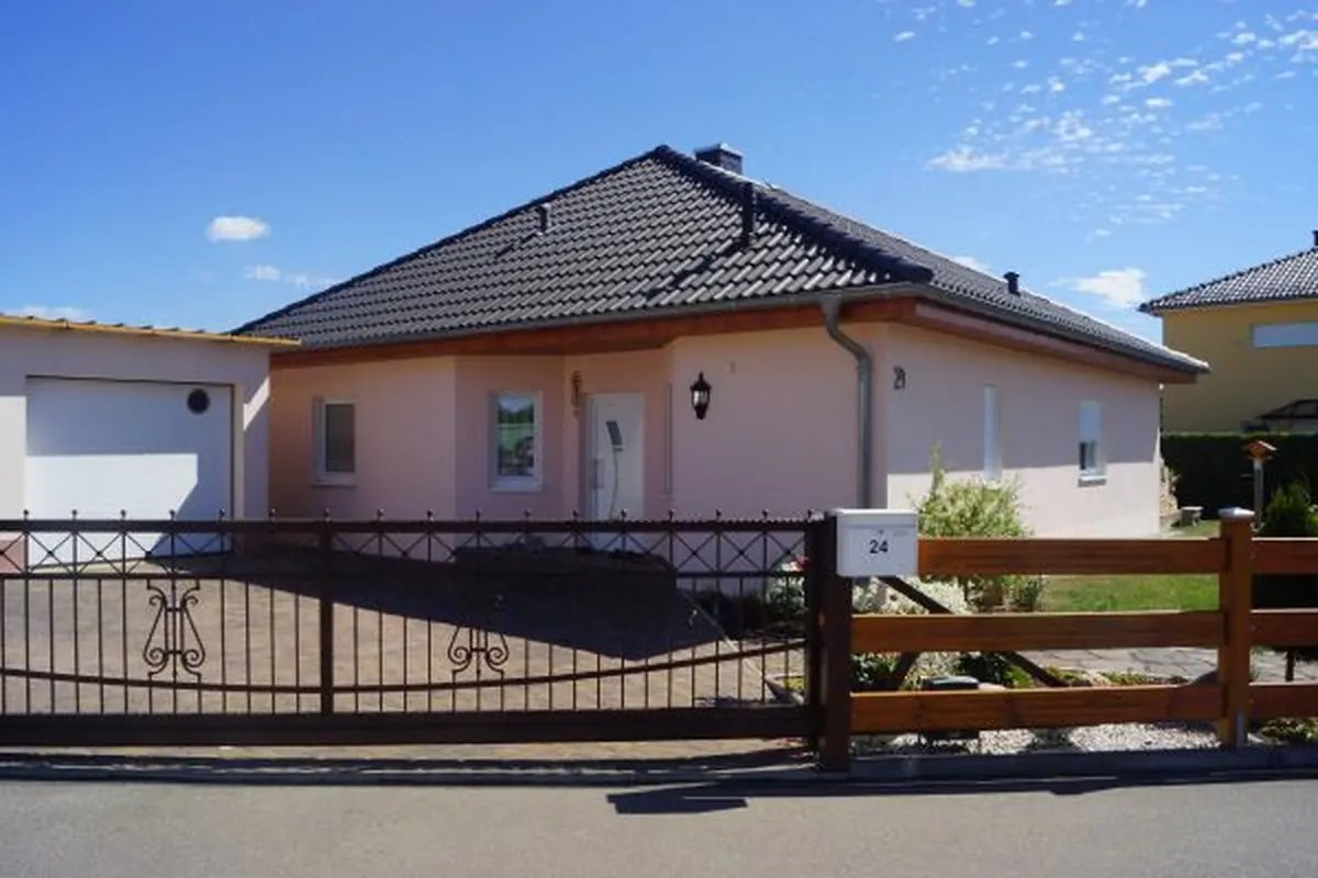 Bungalow Adagio mit dunklem Walmdach hinter schmiedeeisernem Zaun