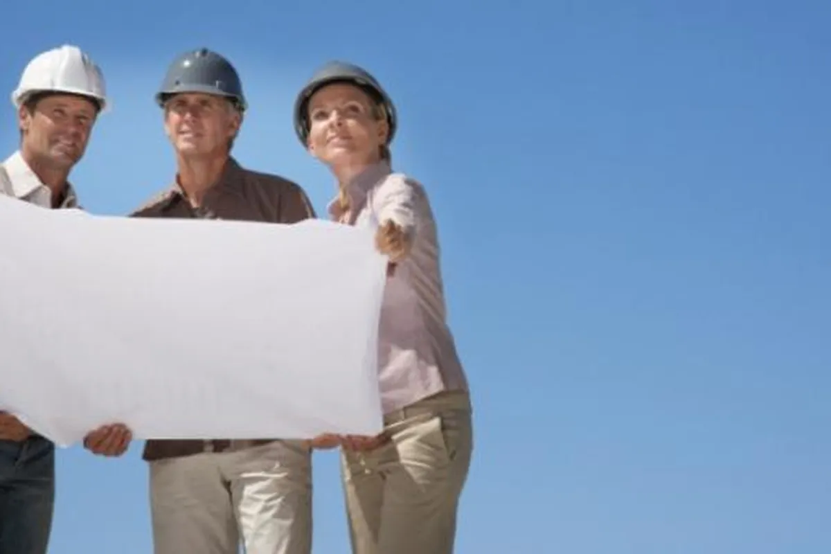 Drei Personen mit Bauhelmen halten auf der Baustelle einen Bauplan